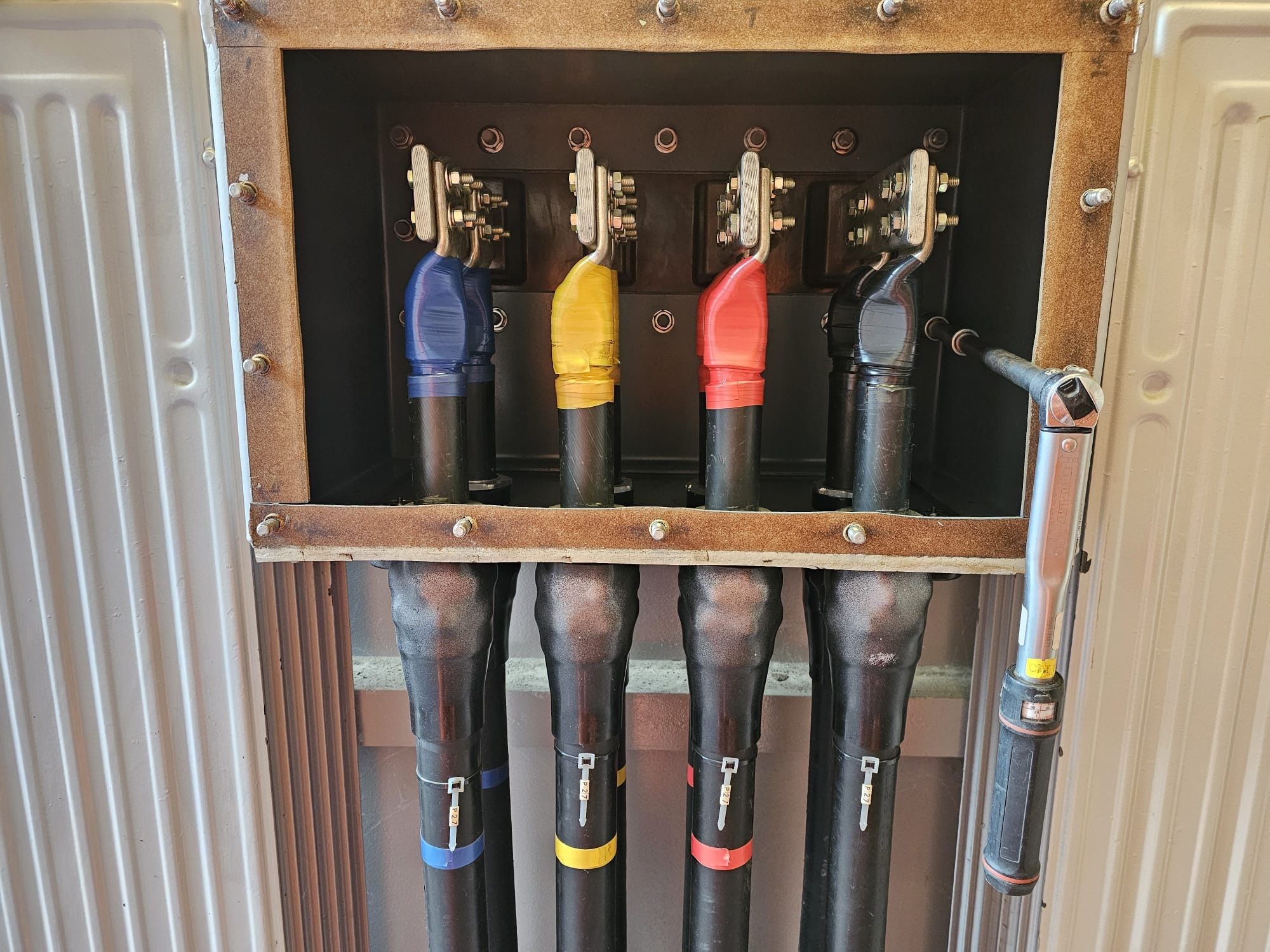 Electrical cable termination box with color-coded cables connected to busbars, supporting safe transformer maintenance practices.