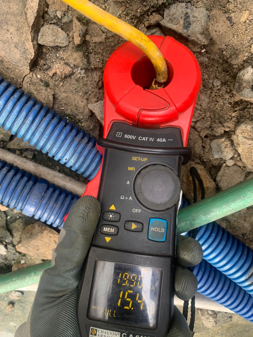 AEMC 6417 clamp meter held by a gloved hand during electrical ground testing on rough earth